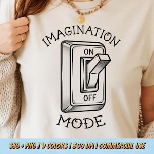 May include: Beige t-shirt with a black and white illustration of a light switch. The switch is in the "ON" position, with the words "IMAGINATION" above and "MODE" below. The shirt is a neutral color.