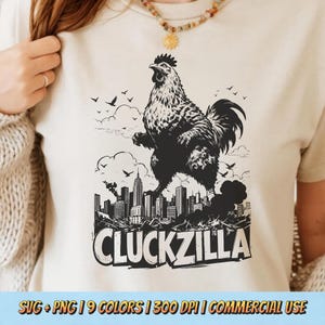 Puede incluir: Una camiseta color crema presenta un gráfico en blanco y negro de un gallo sobre un horizonte urbano, con el texto "CLUCKZILLA" debajo. El diseño incluye pájaros y nubes. La parte inferior de la imagen tiene el texto "SVG + PNG | 9 COLORS | 300 DPI | COMMERCIAL USE".