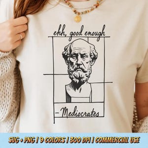 May include: A cream-coloured t-shirt with a black and white drawing of a bust with a beard, framed by lines. The text "ehh, good enough" is above the bust, and "-Mediocrates" is below. The bottom of the image has text.