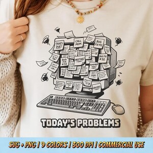 May include: Beige t-shirt featuring a black and white illustration of a vintage computer covered in sticky notes. The notes have text like "Taxes Due!" and "Meeting!" The words "Today's Problems" are printed below the computer.