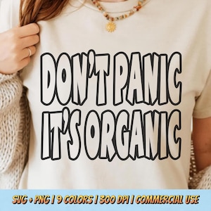 May include: A cream-coloured t-shirt featuring the phrase "DON'T PANIC IT'S ORGANIC" in bold black lettering. The shirt has a crew neck and a simple design. The bottom of the image has text that says "SVG + PNG | 9 COLORS | 300 DPI | COMMERCIAL USE."