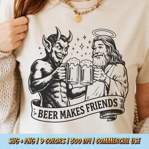 Puede incluir: Camiseta beige con una ilustración en blanco y negro de un diablo y Jesús brindando con jarras de cerveza. La pancarta de abajo dice "BEER MAKES FRIENDS". La camiseta tiene cuello redondo y mangas cortas.