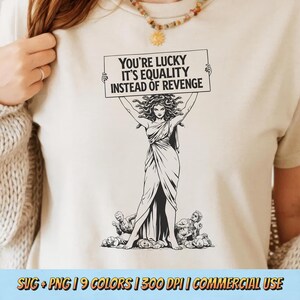 May include: Cream-colored t-shirt featuring a black and white illustration of a woman holding a sign that reads "YOU'RE LUCKY IT'S EQUALITY INSTEAD OF REVENGE." The design includes figures at the bottom. The shirt also has the text "SVG + PNG | 9 COLORS | 300 DPI | COMMERCIAL USE."