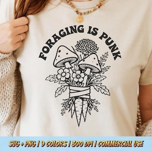 May include: Cream-colored t-shirt featuring a black graphic of mushrooms, flowers, and a carrot bundle, with the text "FORAGING IS PUNK" in a curved font. The shirt has short sleeves and a crew neck.