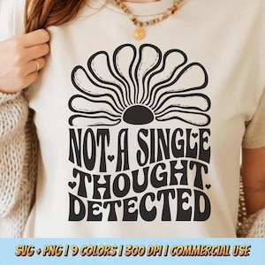 May include: A beige t-shirt with a black graphic that reads "NOT A SINGLE THOUGHT DETECTED" in a retro font. The design includes a stylized sun and hearts. The bottom of the image has text that reads "SVG + PNG | 9 COLORS | 300 DPI | COMMERCIAL USE".