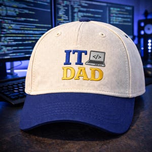 May include: A baseball cap with a cream-colored crown and a blue brim. The cap features the embroidered text "IT DAD" in blue and yellow, with a laptop graphic. The background shows computer screens with code.
