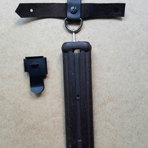 以下が含まれることがあります： 黒い革のベルトループとストラップが付いた、濃い茶色の銃剣鞘。鞘は濃い茶色の素材でできており、金属製の先端が付いています。別の黒い金属クリップも存在します。