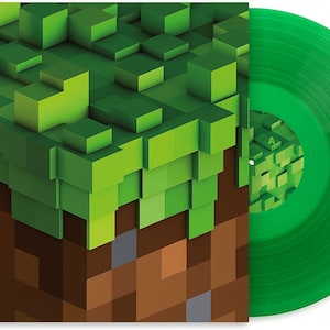 Puede incluir: Un disco de vinilo verde con una portada a juego que presenta un diseño pixelado de bloques verdes y tierra marrón, que recuerda a un videojuego popular. El disco está sobre un fondo blanco.