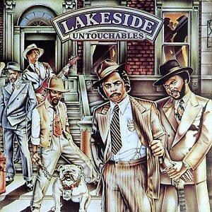 Puede incluir: Portada del álbum "Untouchables" de Lakeside. La imagen presenta a un grupo de hombres con trajes y sombreros, de pie frente a un edificio. El nombre de la banda se muestra en la parte superior. Un perro está en primer plano.
