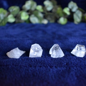 Puede incluir: Cuatro cristales de cuarzo transparentes, cada uno con una forma &uacute;nica, est&aacute;n dispuestos en una fila sobre una superficie de terciopelo azul.