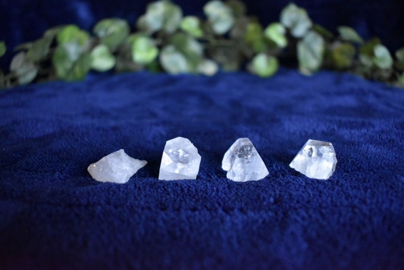 Puede incluir: Cuatro cristales de cuarzo transparentes, cada uno con una forma &uacute;nica, est&aacute;n dispuestos en una fila sobre una superficie de terciopelo azul.