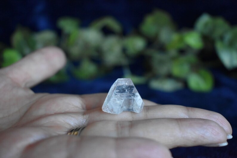 Puede incluir: Un cristal transparente y facetado en forma de pir&aacute;mide, descansando sobre una mano.