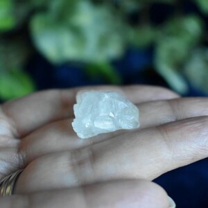 Puede incluir: Un peque&ntilde;o cristal blanco transparente con una textura rugosa y natural. El cristal est&aacute; siendo sostenido en una mano.