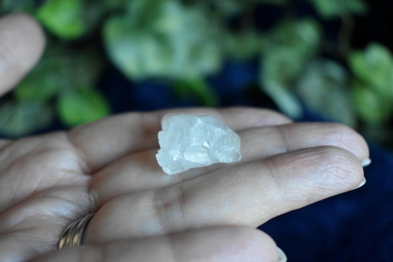 Puede incluir: Un peque&ntilde;o cristal blanco transparente con una textura rugosa y natural. El cristal est&aacute; siendo sostenido en una mano.