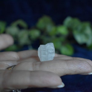 Puede incluir: Un cristal transparente y transl&uacute;cido con una forma geom&eacute;trica, sostenido en una mano. El cristal tiene una apariencia ligeramente nublada y descansa en la palma de la mano.