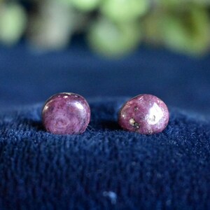 May include: Two round pink and white gemstone earrings. The earrings are on a blue fabric background.
