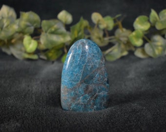 May include: A blue and gray polished gemstone with a smooth, rounded shape. The gemstone is a freeform point and has a natural, organic look.
