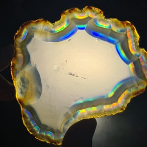 May include: A large, iridescent agate slice with a white center and a scalloped edge. The agate has a rainbow of colors, including red, orange, yellow, green, blue, and purple.