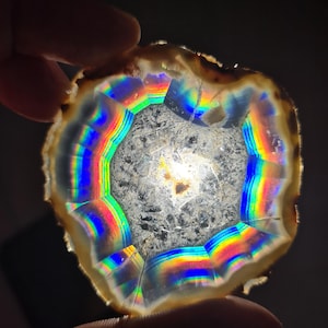 May include: A cross-section of a geode, showcasing a spectrum of colors. The outer edge is a light brown, transitioning to bands of rainbow hues, including red, orange, yellow, green, and blue. The center is a gray, crystalline structure.