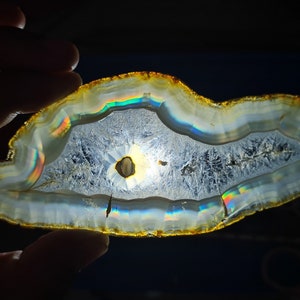 May include: A slice of agate with a rainbow iridescence, displaying the natural patterns and colours of the stone.