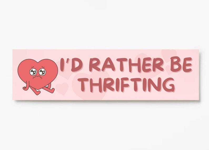 May include: A rectangular sign with a light pink background and the text "I'D RATHER BE THRIFTING" in a reddish-brown font. A cartoon heart with sad eyes and legs is on the left side.