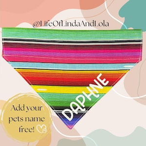 May include: A colorful striped dog bandana with the name "DAPHNE" embroidered on it. The bandana is in a traditional Mexican serape pattern with red, yellow, green, blue, and pink stripes. The text "Add your pets name free!" is written in a circle on the bottom left of the image.