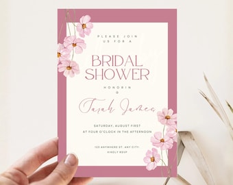 Può includere: Un invito per un addio al nubilato con un bordo malva e accenti floreali. L'invito presenta il testo "BRIDAL SHOWER" e i dettagli dell'evento, tra cui data, ora e luogo. L'invito è tenuto in mano.