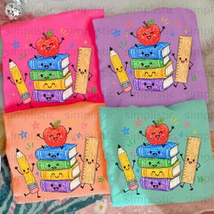 May include: Four t-shirts in pink, purple, orange, and light green, each featuring a graphic of a red apple sitting on a stack of four colorful books, a yellow pencil, and a tan ruler, all with smiling faces and arms, surrounded by small stars.