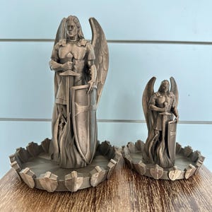May include: Two bronze angel figurines with swords and shields, standing on decorative bases with a shield design.