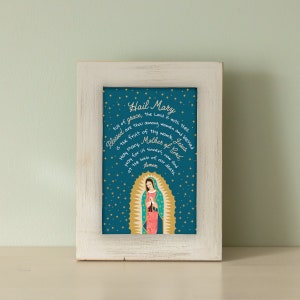 Puede incluir: Una impresi&oacute;n enmarcada con fondo azul y estrellas doradas. La impresi&oacute;n presenta una representaci&oacute;n de la Virgen Mar&iacute;a con el texto "Hail Mary" y una oraci&oacute;n en letras doradas.