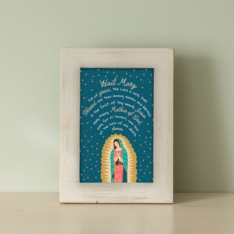 Puede incluir: Una impresi&oacute;n enmarcada con fondo azul y estrellas doradas. La impresi&oacute;n presenta una representaci&oacute;n de la Virgen Mar&iacute;a con el texto "Hail Mary" y una oraci&oacute;n en letras doradas.
