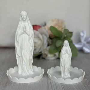 Peut inclure: Deux figurines blanches mates de la Vierge Marie en position de pri&egrave;re, chacune pos&eacute;e sur un plateau circulaire assorti &agrave; bord festonn&eacute;. Les figurines sont r&eacute;alis&eacute;es dans un mat&eacute;riau blanc opaque et solide, avec des robes drap&eacute;es.