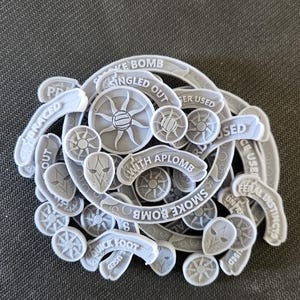 May include: A collection of white plastic game tokens with various text and symbols. The tokens include "Smoke Bomb", "Quick Foot", "With Aplome", "Singled Out", "Feral Instincts", and "Coke Bomb".