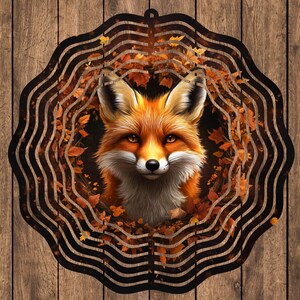 May include: A metal wind spinner with a fox face in the center. The fox is surrounded by a design of swirling leaves in shades of orange, brown, and yellow. The wind spinner is black and has a circular shape.