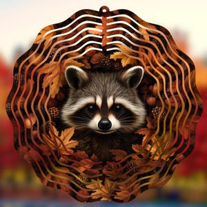 May include: A metal wind spinner with a raccoon face surrounded by autumn leaves and acorns. The raccoon has black eyes and a black nose. The leaves are in shades of brown, orange, and yellow.
