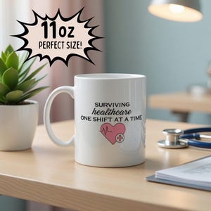 May include: White ceramic mug with the text "SURVIVING healthcare ONE SHIFT AT A TIME" and a pink heart with a medical cross. The mug also has the text "11oz PERFECT SIZE!" in a black speech bubble.