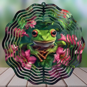 May include: A green and red frog wind spinner with pink flowers and green leaves. The frog is sitting on a branch with its legs crossed. The wind spinner is made of metal and has a circular shape.
