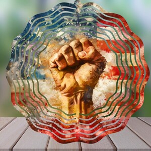 Könnte beinhalten: Ein Wandkunstwerk aus Metall mit einer erhobenen Faust und einem stilisierten amerikanischen Flaggenmuster. Die Flagge ist in Rot-, Weiß- und Blautönen mit einem wellenförmigen Muster gehalten.