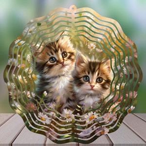 May include: A metal wind spinner with a circular design featuring two brown and white kittens surrounded by white daisies. The background is a blurred green.