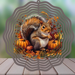 May include: A circular metal wind spinner featuring a central graphic of a brown squirrel surrounded by orange pumpkins and autumn leaves. The outer edge of the spinner has a wavy, concentric cut-out design in a muted grey tone.