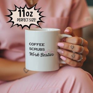 May include: White ceramic mug with the text "COFFEE SCRUBS Work Besties" and a heartbeat graphic. The mug also has the text "11oz PERFECT SIZE!" in a black speech bubble. The mug is held by a person.