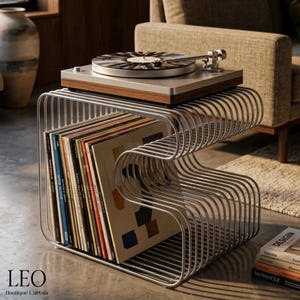 Könnte beinhalten: Ein silbernes, S-förmiges Schallplattenregal aus Metall, das eine Sammlung von Vinylplatten enthält. Auf der Oberseite des Regals steht ein Plattenspieler aus Holz und Silber. Das Regal besteht aus parallel verlaufenden, gebogenen Metallstäben.