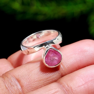 Puede incluir: Un anillo de plata con una gran gema rosa en forma de l&aacute;grima. El anillo tiene una banda lisa y pulida que se curva hacia la gema rosa. La gema es de un rosa vibrante, proporcionando un contraste llamativo con la banda de plata.