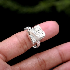 May include: A silver ring with a square-shaped, textured, silver stone.