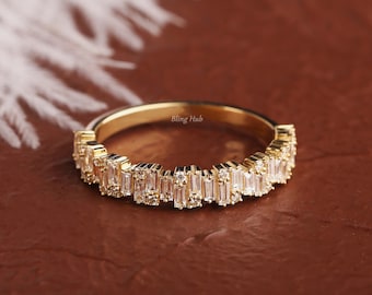 May include: A gold band ring featuring a row of alternating baguette and round cut clear stones. The interior of the band is engraved with the text Bling Hub. The design showcases a textured, multi-level arrangement of stones along the top half.