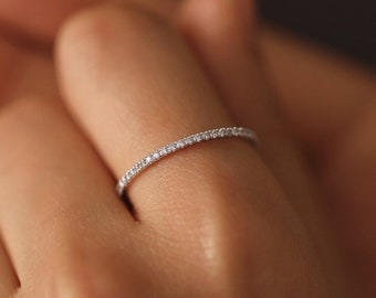 Könnte beinhalten: Ein zarter Silberring mit einer durchgehenden Reihe kleiner, funkelnder, klarer Steine. Der Ring ist dünn und sitzt auf einem Finger, mit einem weichen, unscharfen Hintergrund.