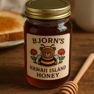 May include: A jar of Bjorn's Hawaii Island Honey with a gold lid. The label features a cartoon bee wearing a bee costume. A wooden honey dipper rests beside the jar. A slice of toast and a mug are in the background.