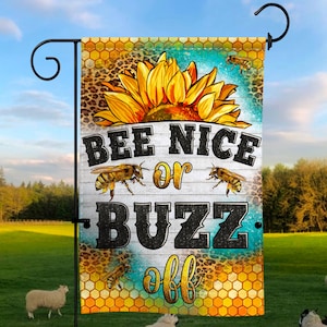 May include: A garden flag with a sunflower and bee design. The flag has the text "BEE NICE or BUZZ off" in black and yellow. The background includes a honeycomb pattern and a leopard print.