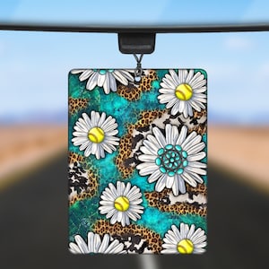May include: Car air freshener with a floral pattern. The design features white daisies with yellow centers and turquoise accents on a turquoise and brown background.