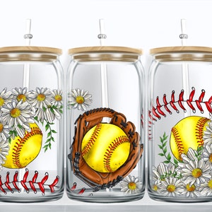 Könnte beinhalten: Drei Glasbecher mit Holzdeckeln und Strohhalmen. Jeder Becher zeigt ein anderes Design: ein Softball mit Gänseblümchen, ein Softball in einem Handschuh mit Gänseblümchen und ein Softball mit roten Nähten und Gänseblümchen.